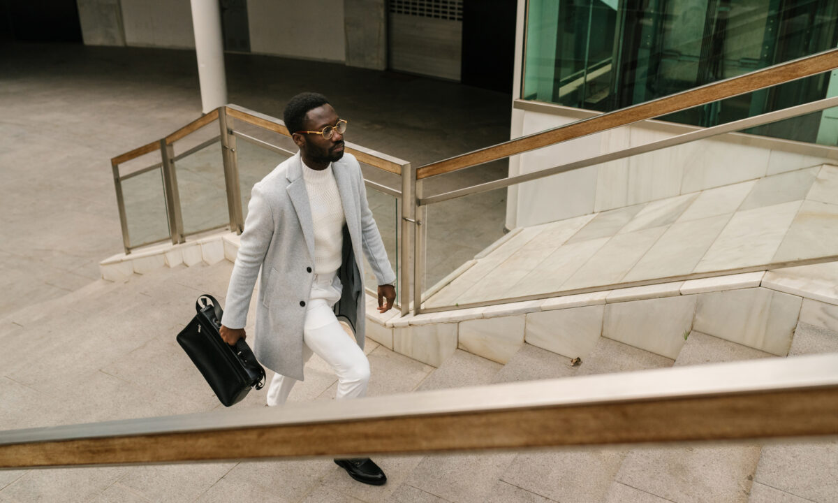 From above of serious African American male entrepreneur in elegant outfit with briefcase walking upstairs of modern business center in city